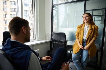 Téléchargez les photos : Jeune femme dans une veste jaune communique avec un collègue au bureau, les gens préfèrent jeans - en image libre de droit
