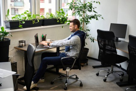Foto de El hombre sonriente trabaja en una cómoda oficina luminosa, usa una computadora portátil - Imagen libre de derechos