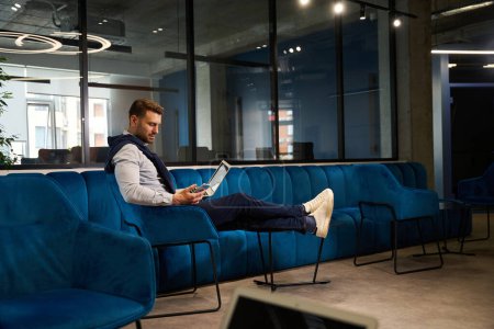 Téléchargez les photos : Homme freelance assis avec un ordinateur portable dans un espace de coworking, il est situé dans un fauteuil confortable - en image libre de droit