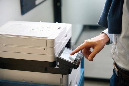 Photo for Employee uses office equipment to work with documents, he is in comfortable casual clothes - Royalty Free Image