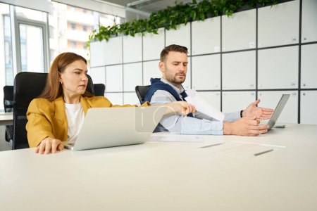 Photo for Quarreling colleagues are sitting at their workplaces, people are located at a large office table - Royalty Free Image