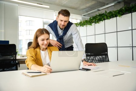 Téléchargez les photos : Jeune femme travaille à un ordinateur portable, le gestionnaire contrôle le travail des employés - en image libre de droit