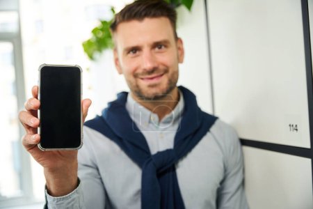 Téléchargez les photos : Jeune homme avec un téléphone portable se tient dans les casiers de stockage dans la zone de coworking bureau - en image libre de droit