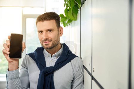 Téléchargez les photos : Un homme avec un téléphone portable se tient dans un casier de stockage dans un bureau de coworking - en image libre de droit