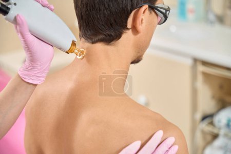Téléchargez les photos : Homme lors d'une séance d'épilation au laser à l'arrière du cou, un professionnel utilise un équipement moderne - en image libre de droit