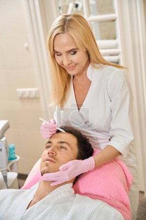Photo for Cosmetologist makes markings on the patients face, a woman uses a special pencil - Royalty Free Image