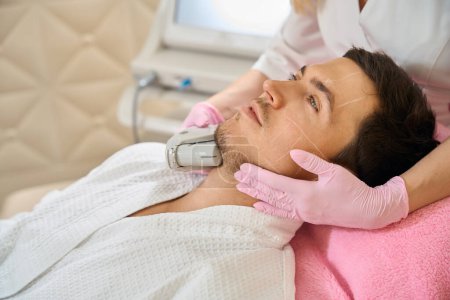 Foto de Especialista realiza elevación de RF microneedle en un cliente en el área de la barbilla, el hombre se sienta en una silla de cosmetología - Imagen libre de derechos