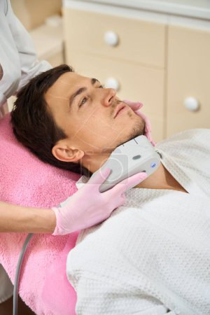 Photo for Handsome man undergoing microneedle RF lifting procedure in the chin area, the specialist works in protective gloves - Royalty Free Image