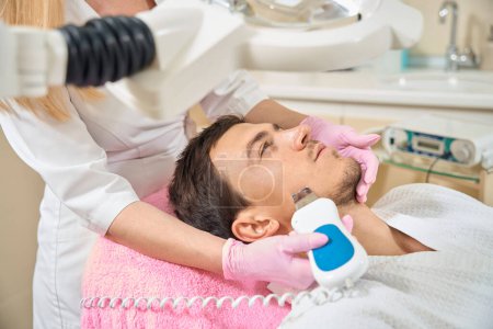 Téléchargez les photos : Beau homme subissant un nettoyage facial par ultrasons, spécialiste des gants de protection - en image libre de droit