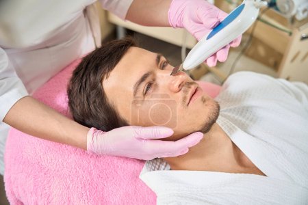 Téléchargez les photos : Homme sur un nettoyage efficace du visage par ultrasons, un spécialiste utilise un appareil moderne - en image libre de droit