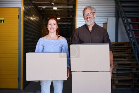 Photo for Happy couple is in a storage warehouse, people have cardboard boxes with things - Royalty Free Image