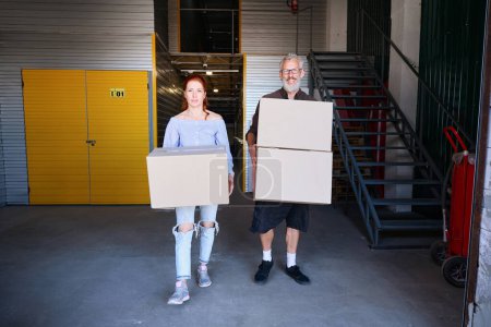 Foto de Un hombre y una mujer llevan cajas de cartón con cosas, están en un almacén. - Imagen libre de derechos