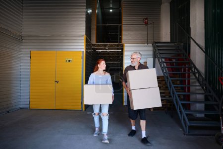 Téléchargez les photos : Heureux couple d'âge moyen est dans un entrepôt de stockage, les gens ont des boîtes en carton avec des choses - en image libre de droit