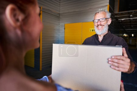Photo for Red-haired woman is in a storage warehouse with her companion, people have cardboard boxes with things - Royalty Free Image