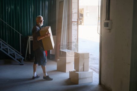 Téléchargez les photos : L'homme barbu porte des boîtes en carton, il est dans un entrepôt - en image libre de droit