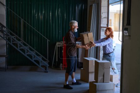 Téléchargez les photos : Femme souriante aide son mari à transporter des boîtes avec des choses, les gens sont dans un entrepôt - en image libre de droit