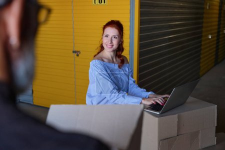 Téléchargez les photos : Homme et femme cheveux gris communiquent dans un entrepôt de stockage, la femme utilise un ordinateur portable - en image libre de droit