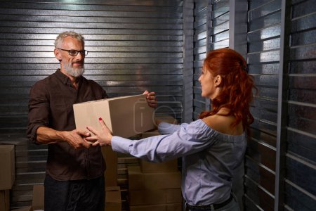 Photo for Spouses loading cardboard boxes with things into a storage container, a married couple is in a warehouse - Royalty Free Image