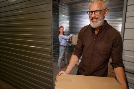 Téléchargez les photos : Femme aidant un homme à charger des boîtes avec des choses pour le stockage, un couple marié est dans un entrepôt - en image libre de droit