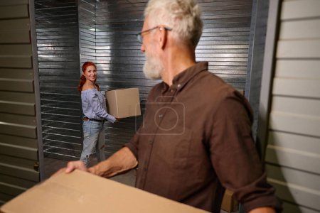 Foto de El hombre ayuda a una mujer a cargar cajas con cosas para almacenar, una pareja casada está en un almacén - Imagen libre de derechos