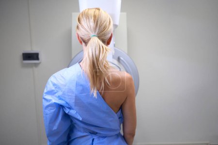 Photo for Back view of adult woman standing in front of mammography unit in radiology room - Royalty Free Image