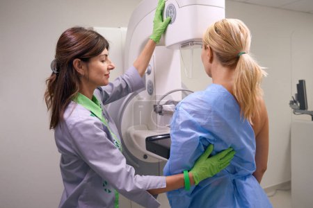 Téléchargez les photos : Technologue en radiologie commande panneau de commande sur la machine de mammographie pour positionner la pagaie de compression contre la paroi thoracique du patient - en image libre de droit