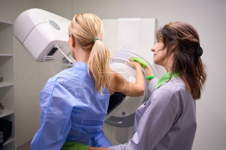 Foto de Mamógrafo descansando el brazo del paciente con el codo doblado a través de la parte superior del receptor en la unidad de mamografía - Imagen libre de derechos