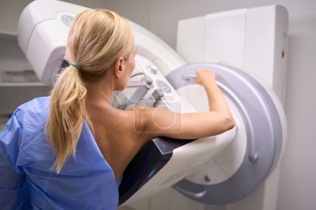 Photo for Back view of Caucasian female patient undergoing 3D mammography in radiology room - Royalty Free Image