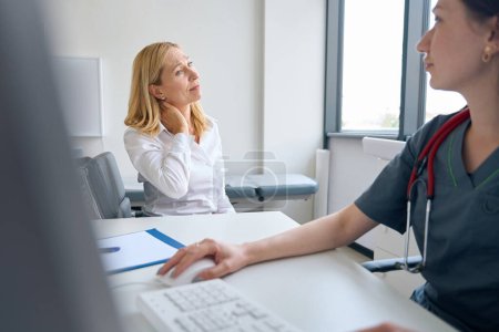 Téléchargez les photos : Femme bouleversée assise au bureau avant que le neurologue touche le côté du cou avec la main pendant la consultation médicale - en image libre de droit