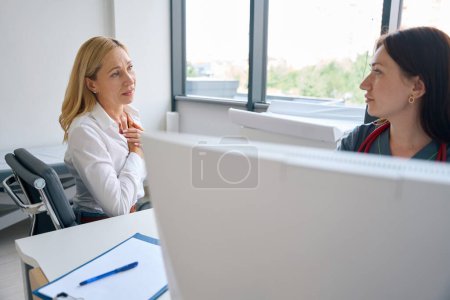 Téléchargez les photos : Patient cardiaque effrayé assis au bureau devant un médecin parlant de l'inconfort dans la région thoracique - en image libre de droit