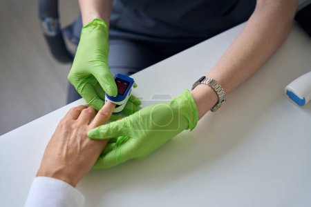 Foto de Foto recortada del médico sentado en el escritorio colocando oxímetro de pulso en la punta del dedo del paciente - Imagen libre de derechos