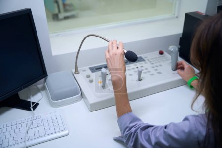 Photo for Cropped photo of radiologic technologist seated at desk touching microphone and joystick on console - Royalty Free Image