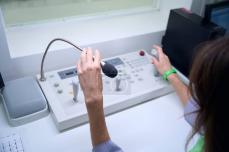 Photo for Cropped photo of radiographer seated at desk touching microphone while moving joystick on console in control room - Royalty Free Image