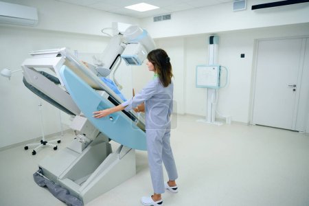 Photo for Radiographer tilting radiographic table with female in supine position towards x-ray tube - Royalty Free Image