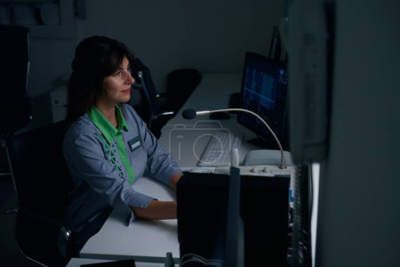 Foto de Radiógrafo concentrado sentado en el escritorio frente a la consola de operaciones mirando a la distancia - Imagen libre de derechos