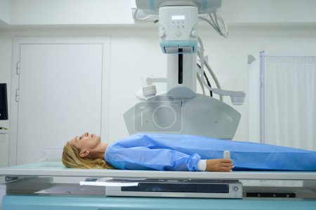 Foto de Vista lateral de la mujer adulta en vestido acostado supino en la mesa de rayos X durante el examen radiográfico - Imagen libre de derechos