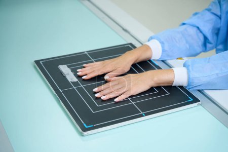 Téléchargez les photos : Photo recadrée d'un patient posant ses mains avec une surface palmaire sur un récepteur d'image sur une table à rayons X - en image libre de droit