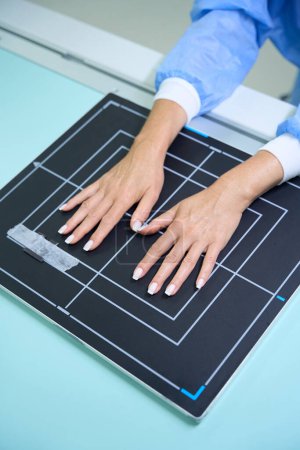 Téléchargez les photos : Photo recadrée de la personne positionnant les mains avec une surface palmaire sur le récepteur d'image sur la table radiographique - en image libre de droit