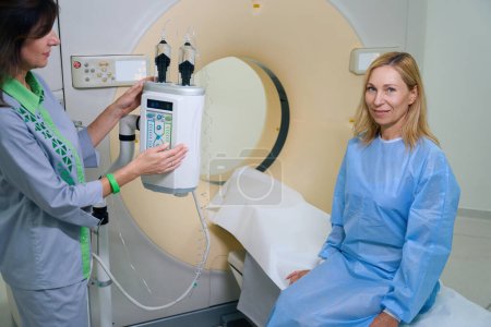 Foto de Técnico radiológico experimentado preparando a la mujer adulta para la tomografía computarizada con medios de contraste - Imagen libre de derechos