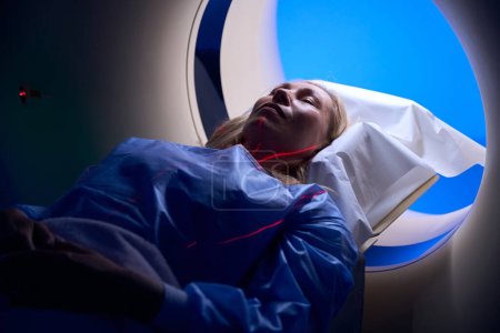 Foto de Mujer acostada en decúbito supino con brazos en el abdomen en la mesa de examen colocada dentro del pórtico del escáner CT - Imagen libre de derechos