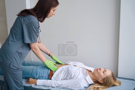 Photo for Focused general practitioner palpating female patient abdomen lying in supine position on examination couch - Royalty Free Image