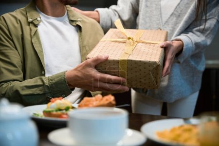 Foto de Hombre desconocido recibe caja de regalo de la mujer disfrutando de la celebración de Año Nuevo y la cena festiva en casa - Imagen libre de derechos