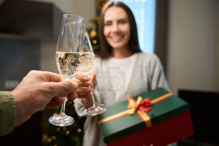 Photo for Woman clinking glass of champagne with unrecognizable man enjoying Christmas and New Year celebration - Royalty Free Image