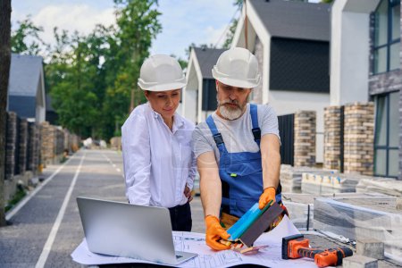 Photo for Builder holding paint sample boards over architectural drawing in front of architectural designer on building site - Royalty Free Image