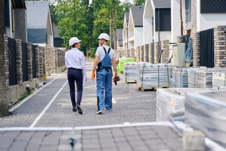 Photo for Back view of building inspector and builder walking along street between rows of unfinished residential houses - Royalty Free Image