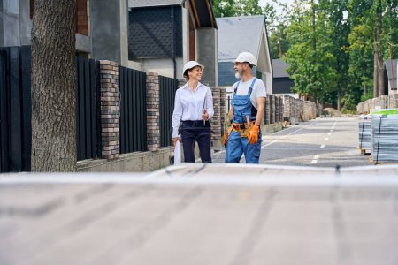 Photo for Joyous site supervisor and builder standing on street in front of unfinished cottage during conversation - Royalty Free Image
