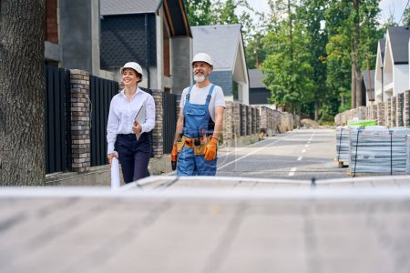 Photo for Cheerful building inspector and builder standing on street in front of unfinished house - Royalty Free Image