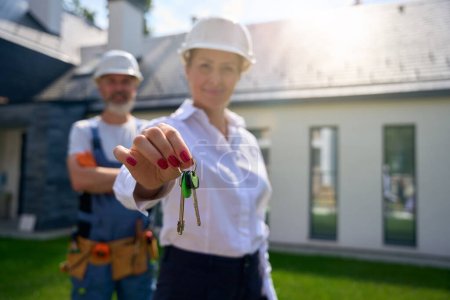 Photo for Construction supervisor demonstrating bunch of house keys in hand with standing outside cottage with contractor on background - Royalty Free Image