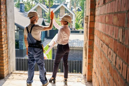 Photo for Cheerful building inspector giving high-five to contented builder while standing inside unfinished residential house - Royalty Free Image