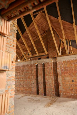 Photo for Interior view of unfinished attic room with red brick walls and timber roof trusses - Royalty Free Image